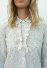 Camisa de lino con estampado floral en tonos pasteles, cuello camisero, manga larga y detalle de jabot con encaje color natural en la parte delantera.