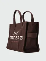 Bolso tipo tote de lona color marrón chocolate, con doble asa superior y estampado frontal con el nombre del modelo y la marca en color blanco.