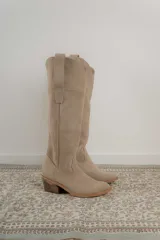Bota estilo tejana de caña alta, confeccionada en gamuza, con taco cuadrado y diseño de costuras decorativas.