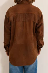 Camisa tipo overshirt de gamuza marrón óxido con flecos en el pecho, cuello camisero, bolsillos delanteros y cierre frontal de botones metálicos a presión.