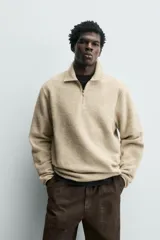 Sudadera de corte relajado confeccionada en tejido con textura, color beige. Presenta cuello solapa con cierre frontal de cremallera, manga larga y acabados con cinta elástica en puños y ruedo.