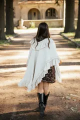 Ruana de lana merino color crudo, con diseño de silueta amplia y caída fluida. Presenta detalles de volados en lino a lo largo de la prenda y terminaciones con flecos en el ruedo.