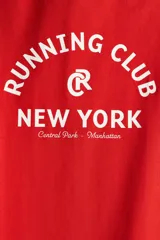 Remera de algodón color rojo, con cuello redondo y manga corta. Presenta un estampado frontal en blanco con el texto "Running Club New York Central Park - Manhattan" y un logo circular con una 'R' en el centro.