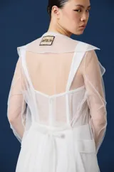 Trench largo de mujer confeccionado en tul transparente, con cuello camisero, mangas largas y frente abierto. Presenta una caída fluida y ligera, ideal para superponer sobre otras prendas.