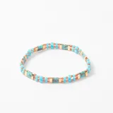 Pulsera elástica de doble hilera compuesta por cuentas turquesas, cuentas cilíndricas de piedra turquesa con vetas marrones y separadores metálicos dorados.