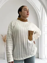 Polera blanca de tejido trenzado con cuello alto de cuero marrón y bolsillo de cuero marrón con textura de cocodrilo.