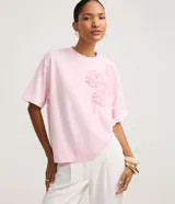 Blusa boxy de manga corta, confeccionada en algodón, con cuello redondo y detalles de flores de tejido aplicadas en el hombro y sisa.