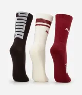 Kit de tres pares de medias deportivas Puma de caña larga. Un par es beige con dos rayas marrones y logo de Puma. Otro par es blanco liso. El tercer par es marrón oscuro con dos rayas blancas y logo de Puma. Todas están confeccionadas en algodón.
