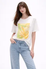 Remera de algodón color blanco, de corte holgado y manga corta, con cuello a la base. Presenta un estampado frontal rectangular en tonos amarillos y verdes con motivos botánicos, realzado con detalles bordados y lentejuelas.