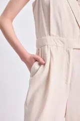 Mono largo color crudo de lino, con cuello en V, sin mangas, corte a la cintura con botón y pantalón de corte recto.