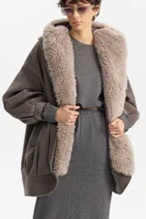 Chaqueta amplia de silueta balloon en color gris, con capucha integrada y solapa interior revestida en piel sintética tipo peluche. Presenta mangas largas con puños elásticos y un diseño envolvente y relajado.