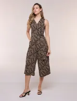 Enterito cropped con caída fluida, sin mangas y con escote en V cruzado estilo wrap. Presenta un lazo lateral para anudar en la cintura, bolsillos prácticos y pantalón midi de corte amplio con diseño geométrico en tonos negro y beige.