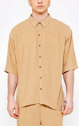 Camisa de corte oversize, color beige, con cuello clásico, cierre frontal de botones y mangas cortas. Confeccionada en tejido de lino.