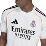 Camiseta de fútbol Adidas del Real Madrid, modelo primera equipación temporada 25/26. Diseño blanco con detalles en negro y dorado. Incluye logo de Adidas, escudo del club y sponsor Emirates Fly Better en el frente.