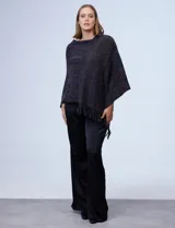 Poncho tejido en hilo soft, con efecto jaspeado multicolor (predominantemente tonos oscuros como azul marino, negro, y toques de violeta y dorado/lurex). Presenta un diseño asimétrico y flecos largos en los bordes.