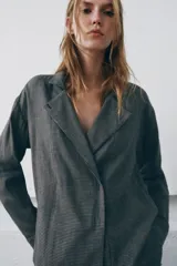 Camisa de corte oversize confeccionada en algodón, con estampado de cuadros pequeños en tonos grises. Presenta cuello solapa, cierre frontal con botones ocultos y mangas largas con puños rectos.