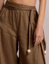Pantalón palazzo de lino color azul, de tiro alto con cintura elastizada y cinto lazo incorporado con cuentas decorativas en las puntas. Presenta aberturas laterales pronunciadas en las piernas y corte amplio.