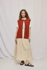Chaleco de punto color beige, sin mangas, con escote redondo y cierre frontal con botones carey. Presenta diseño calado y silueta amplia.