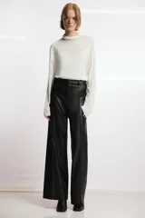 Pantalón de tiro alto efecto piel en color marrón, con pierna ancha y costuras marcadas en la parte delantera. Presenta trabillas en la cintura y cierre frontal con cremallera, botón y gancho metálico.