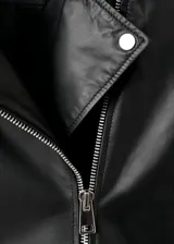 Chaqueta estilo biker de cuero negro, con cuello de solapa con muescas, cierre frontal cruzado con cremallera, bolsillos laterales con cremallera y un bolsillo pequeño con solapa y broche a presión.