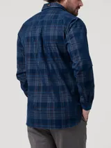 Camisa de manga larga confeccionada en algodón orgánico con textura de cotelé. Presenta un diseño de cuadros escoceses en tonos azules y marrones, cuello clásico, cierre frontal con botones y dos bolsillos en el pecho.