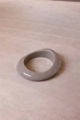 Pulsera rígida de resina con diseño orgánico y acabado brillante, disponible en colores marrón, gris y naranja.