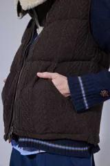 Chaleco tejido de punto color marrón con cuello de piel sintética, cierre frontal con cursor de cuero y diseño acolchado con cortes horizontales.
