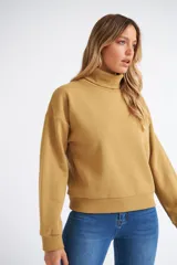 Buzo tipo polera de algodón, con cuello alto, mangas largas con puños y diseño holgado. Presenta una pequeña grifa metálica decorativa.