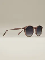 Anteojos de sol con armazón negro mate y forma redonda. Lentes con filtro degradado oscuro.