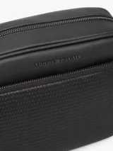 Bandolera Tommy Hilfiger de color negro, confeccionada en poliuretano con diseño de compartimento principal con cierre de cremallera y bolsillo exterior frontal con panel de textura tejida. Cuenta con correa ajustable, bolsillo interior con cierre y detalles distintivos de la marca con logo metálico en la parte delantera.