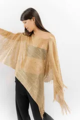 Poncho de tejido de punto metalizado en color dorado, con diseño amplio y flecos en el borde inferior. Presenta apliques sutiles de piedras y un estilo holgado.