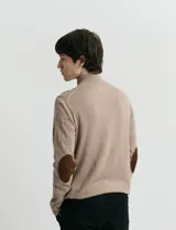 Sweater de punto color verde oliva, con cuello alto y medio cierre frontal. Presenta coderas en símil nappa y puños acanalados.