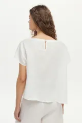 Blusa de lino color blanco, con cuello bote y mangas cortas de corte holgado.