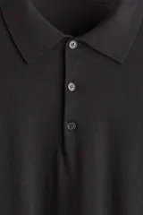 Remera polo de manga larga en punto fino negro, con cuello clásico y tapeta de tres botones. Presenta remates acanalados en puños y bajo.