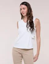 Chaleco blanco sin mangas de estilo smart-casual, con escote en V y costuras verticales de entalle. Cuenta con bolsillos o solapas simuladas a los lados de la cintura decorados con un botón metálico dorado y un largo a la cadera.