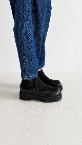 Bota tipo chelsea de caña baja, confeccionada en una combinación de cuero liso y gamuza negra. Presenta una suela track robusta y punta cuadrada.