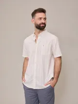 Camisa de manga corta para hombre, color blanco con rayas verticales finas en relieve. Tiene cuello abotonado, bolsillo en el pecho izquierdo y logo bordado pequeño.