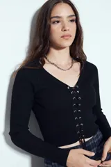 Top de tejido acanalado color negro, con escote en V y cierre frontal mediante cordones ajustables con ojales metálicos. Presenta mangas largas y un corte entallado al cuerpo.