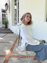 Cartera tipo sobre color crudo, confeccionada en cuero, con correa larga de cuero marrón y costuras decorativas en contraste.