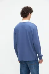Remera polo de manga larga azul con cuello camisero blanco y cierre frontal de botones ocultos. Presenta un pequeño bordado con el texto "uniform" en el pecho y calce relajado.