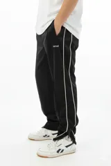 Pantalón de jogging negro con vivo lateral doble blanco, corte holgado, tiro medio, botamanga elastizada y cierres en los tobillos.