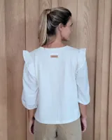 Remera blanca de algodón con cuello redondo, mangas tres cuartos abullonadas y detalle de volados en los hombros.