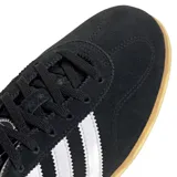 Championes Adidas modelo Gazelle Lo Pro W, color negro con tres franjas laterales blancas y logo dorado. Tienen cordones negros y suela de goma color caramelo translúcida.