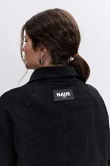 Campera de denim negro con cierre frontal y botones a presión, cuello clásico y bolsillos laterales.