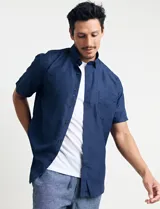 Camisa de manga corta azul con estampado de lunares blancos, cuello abotonado y bolsillo en el pecho.