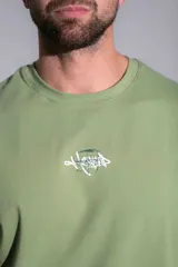 Remera oversize de algodón elastizado color verde militar, con cuello redondo, mangas cortas y diseño gráfico bordado en el pecho.