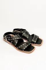 Sandalias bajas de cuero negro con tachas plateadas, tiras cruzadas y hebilla al tobillo.