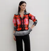 Camisa de manga larga con cuello solapa y cierre frontal de botones. Presenta un diseño estampado con bloques geométricos en tonos azul, blanco y negro.
