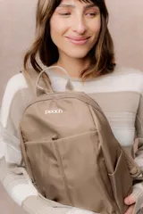 Mochila de diseño minimalista y compacto color tostado, con múltiples compartimentos, bolsillos laterales, bolsillo frontal con cierre oculto, correas regulables y logo metálico de la marca Peach en la parte frontal.