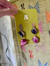 Aros colgantes elaborados con base rectangular de alpaca texturizada, de la cual cuelgan dos piedras de nácar en tonos azul oscuro y fucsia.